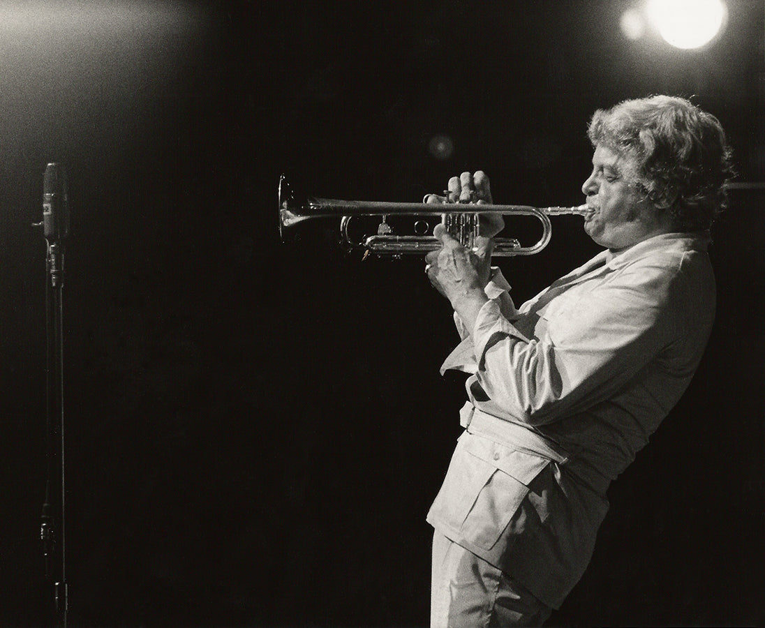 Maynard Ferguson playing a trumpet on stage with a microphone and spotlight in the background